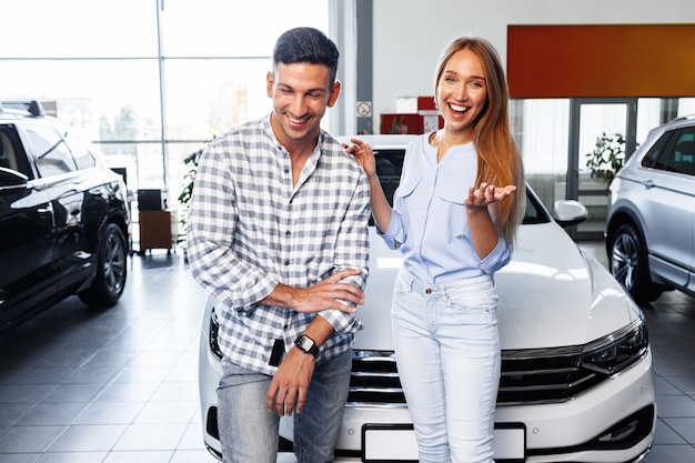 Cherrful pareja joven en el concesionario comprando un coche nuevo
