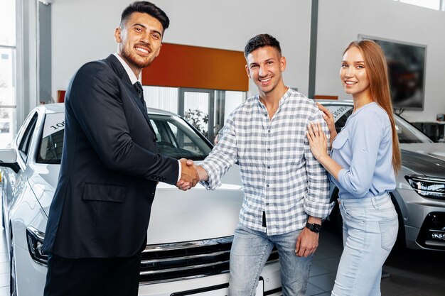 Cherrful pareja joven en el concesionario comprando un coche nuevo