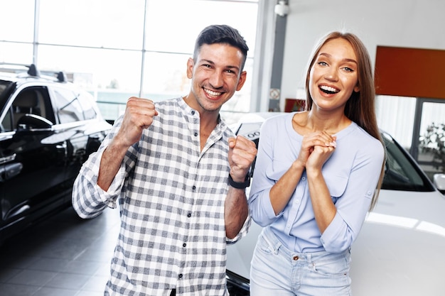 Cherrful pareja joven en el concesionario comprando un coche nuevo