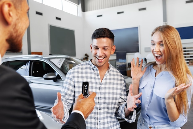 Cherrful pareja joven en el concesionario comprando un coche nuevo