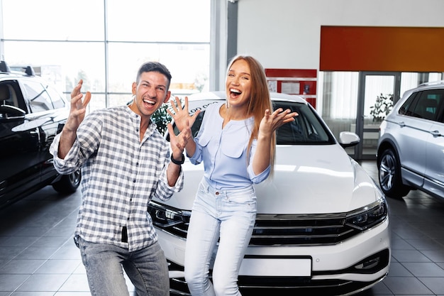 Cherrful pareja joven en el concesionario comprando un coche nuevo