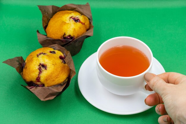 Cherry Muffins mit einer Tasse Tee auf grünem Hintergrund Closeup Cherry Muffins Womans Hand