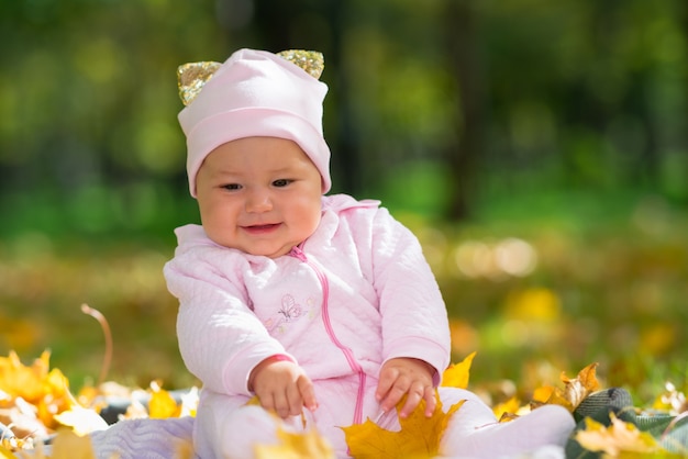 Cherubic Little Baby Girl jugando con hojas de colores en un parque de otoño mientras se sienta en una alfombra en el césped en un ángulo de visión baja