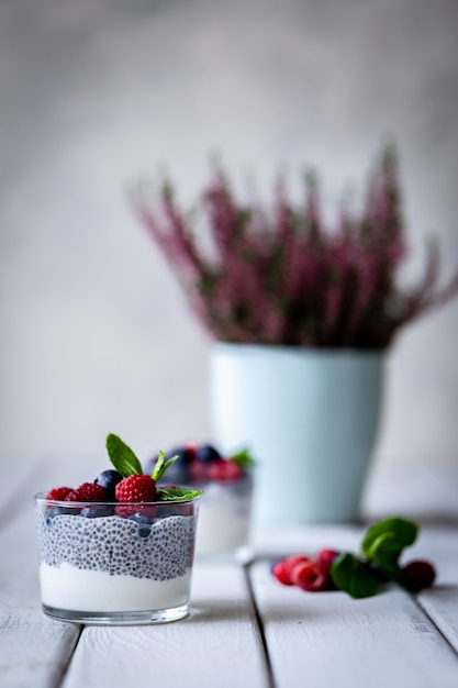 Chia com frutos silvestres. Framboesas e mirtilos. Sobremesa deliciosa e saudável e flores violetas sobre uma mesa rústica de madeira branca.