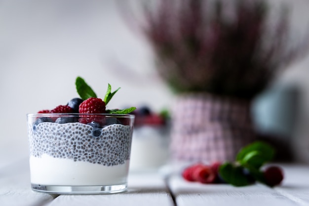 Chia com frutos silvestres. Framboesas e mirtilos. Sobremesa deliciosa e saudável e flores violetas sobre uma mesa rústica de madeira branca.