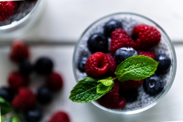 Chia com frutos silvestres. Framboesas e mirtilos. Sobremesa deliciosa e saudável sobre uma mesa rústica de madeira branca. Ponto de vista Zenith