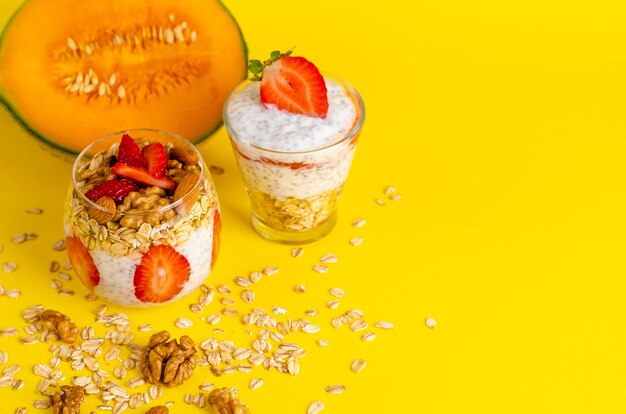 Chia-Joghurtpudding mit Erdbeeren, Haferflocken und Nüssen in einem Glas auf Gelb