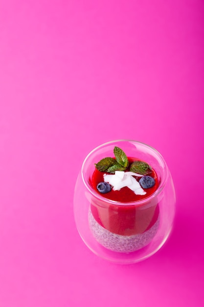 Chia-Pudding mit Beerenpüree im Glas auf rosa Hintergrund