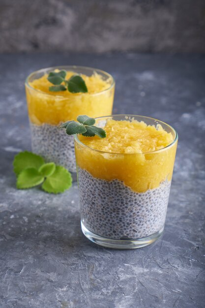 Chia Pudding mit Mango und Minze im Glas auf grauem Tisch