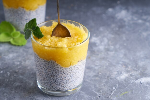 Chia Pudding mit Mango und Minze im Glas auf grauem Tisch