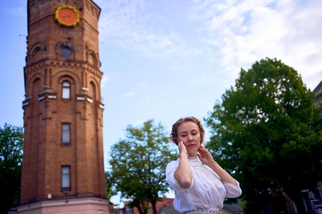 Foto chic mujer joven en un vestido vintage blanco en la plaza cerca de la histórica torre de agua en vinnytsia