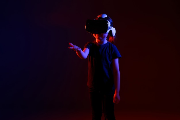 Chica de 5 años experimentando el juego de auriculares VR en una superficie colorida. Niño usando un dispositivo de juego para realidad virtual. Gafas futuristas a temprana edad. Tecnología virtual.