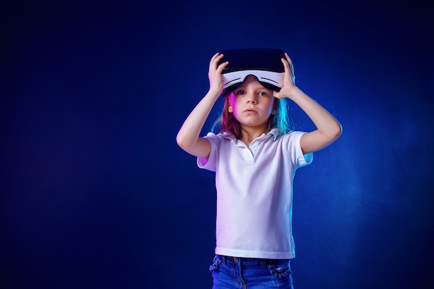 Chica de 7 años que experimenta el juego de auriculares VR en colores. Niño usando un dispositivo de juego para realidad virtual. Lo recogí y cuestioné