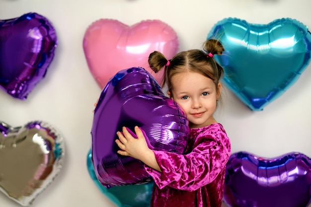 Chica abraza un globo morado en forma de corazón en la zona de fotos de corazones para el día de San Valentín