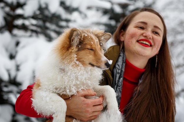 Chica abraza a Sheltie en el fondo de los árboles de invierno.