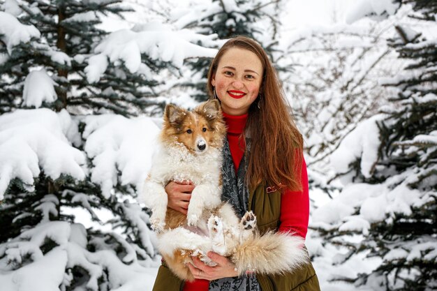 Chica abraza a Sheltie en el fondo de los árboles de invierno.