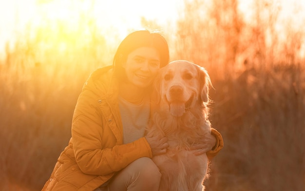 Chica abrazando a perro golden retriever con luz del atardecer al aire libre. Mujer joven acariciar a perro labrador mascota en la naturaleza en otoño