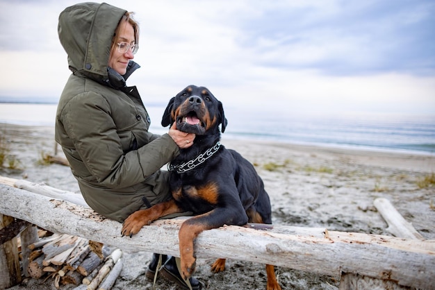 Chica abrazando a un perro Rottweiler en la playa