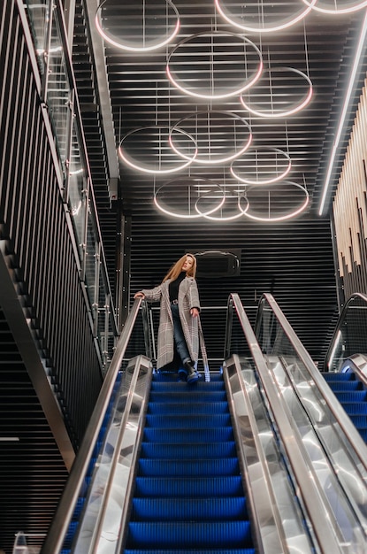 una chica con abrigo baja por la escalera mecánica