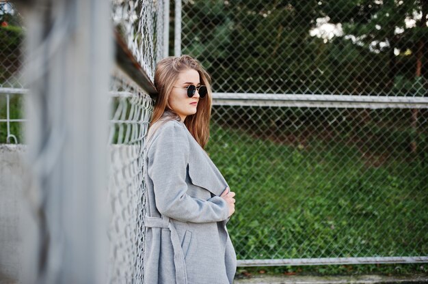 Chica en abrigo gris con gafas de sol en el pequeño estadio de la calle.