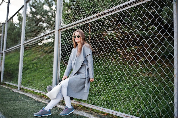 Chica con abrigo gris con gafas de sol en un pequeño estadio callejero