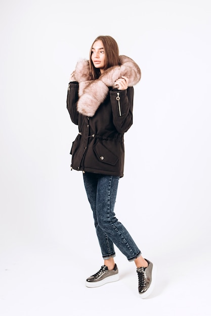 Chica en un abrigo de invierno con cuello de piel sobre un fondo blanco.