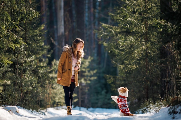 Una chica con un abrigo y un perro de raza Jack Russell Terrier con un suéter de punto de Año Nuevo en un bosque de abetos de invierno en la nieve Concepto de Navidad