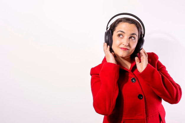 Chica con abrigo rojo y auriculares escuchando música fondo blanco con espacio de copia