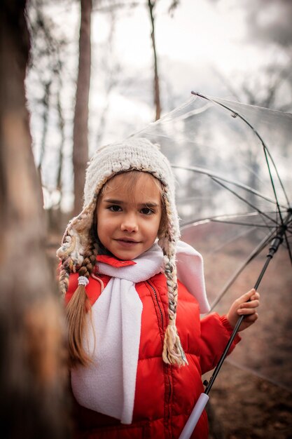 Chica de abrigo rojo con paraguas transparente caminando sola en el bosque de la primavera