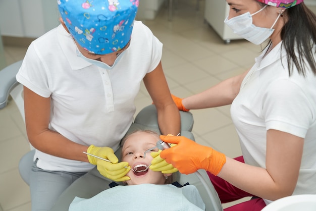 Chica acostada en una silla con la boca abierta y mirando a los dentistas