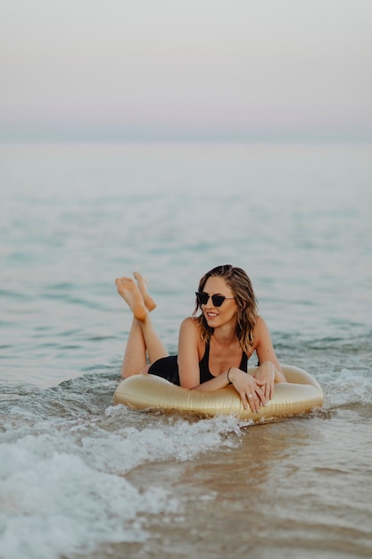 Chica acostada sobre un tubo de oro para nadar en la playa.