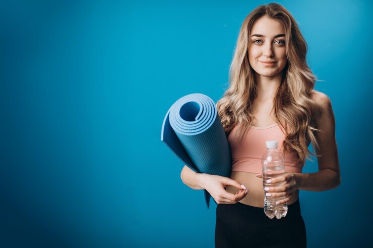 Chica activa sosteniendo colchoneta de yoga y botella de agua en el estudio