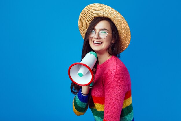 Chica activista lgbt en suéter de arco iris hablando en megáfono y sonriendo