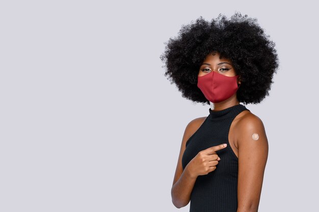 Chica adolescente afro muestra felizmente la marca de la vacuna en gris de fondo