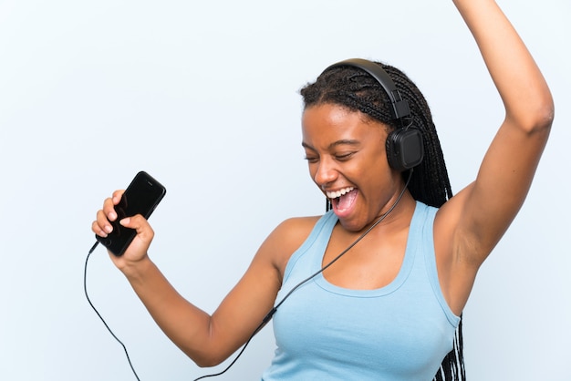 Chica adolescente afroamericana con cabello largo trenzado escuchando música con un móvil y bailando