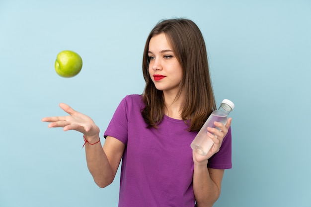 Chica adolescente aislada en la pared azul con una manzana y con una botella de agua