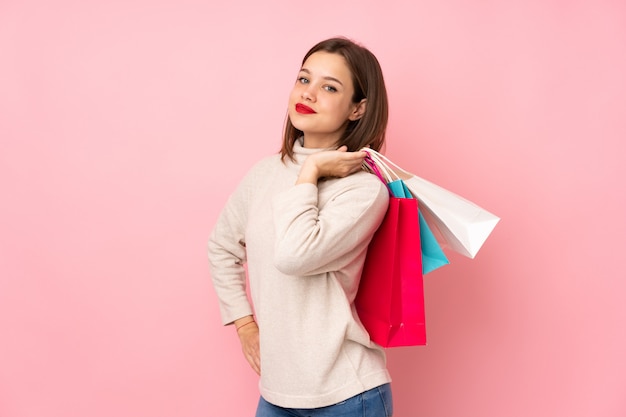 Chica adolescente aislada en la pared rosa sosteniendo bolsas de compras y sonriendo