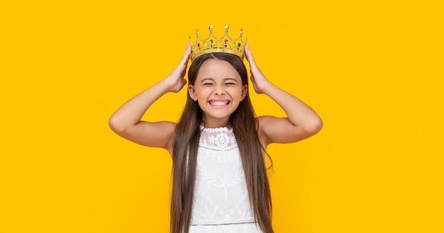 Chica adolescente alegre en corona sobre fondo amarillo