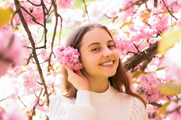 Chica adolescente alegre en la flor de sakura florece en primavera