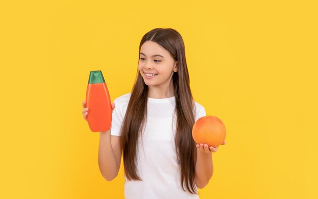 Chica adolescente alegre pelo largo con loción corporal y pomelo sobre vitamina de fondo amarillo