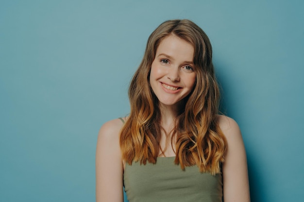 Chica adolescente alegre positiva en el tanque superior que demuestra optimismo y felicidad aislada sobre la pared azul