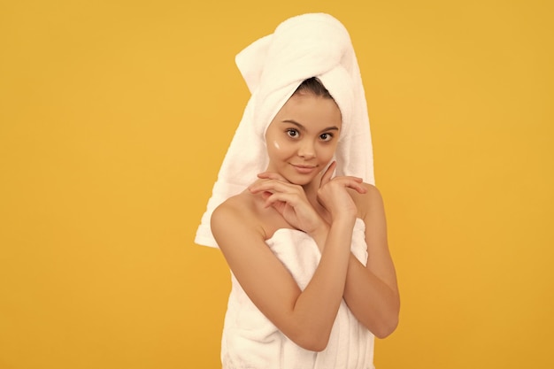 chica adolescente alegre en una toalla de ducha con crema en la cara