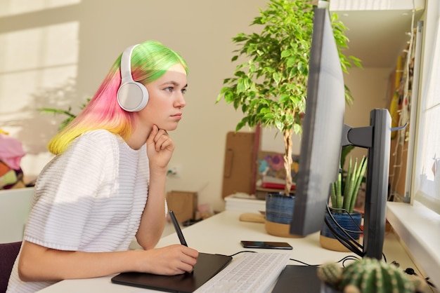 Chica adolescente artista en auriculares sentada en la mesa en casa dibujando en la computadora usando tableta gráfica Pasatiempos y ocio de estudiante universitario creativo
