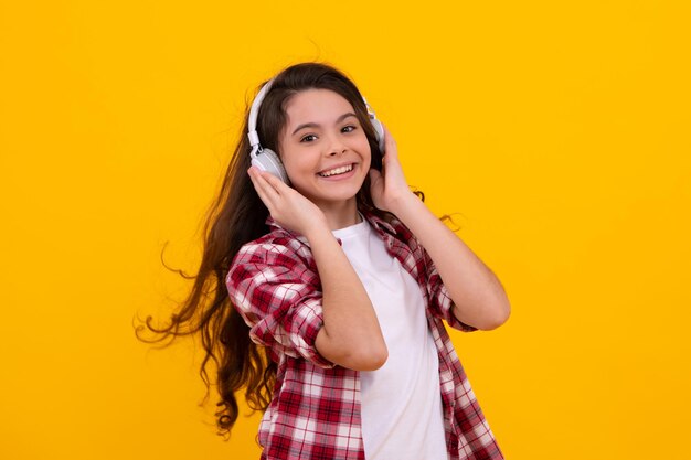 Chica adolescente en auriculares escucha música Accesorio de dispositivo de auricular inalámbrico Niño disfruta de la música en auriculares sobre fondo amarillo Adolescente casual feliz