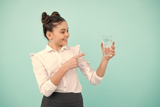 Chica adolescente bebiendo agua de vidrio sobre fondo azul Salud de la vida diaria Beber agua para el cuidado de la salud y el equilibrio corporal Deshidratación de niños sedientos