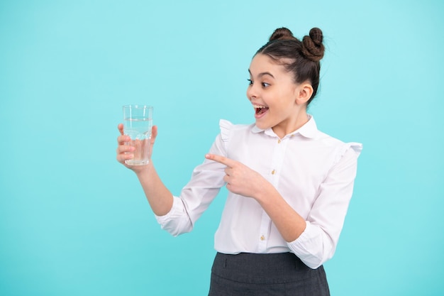 Chica adolescente bebiendo agua de vidrio sobre fondo azul Salud de la vida diaria Beber agua para la salud