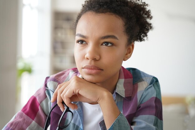 Chica adolescente birracial pensativa sostiene gafas mira a un lado le da descanso a sus ojos cansados perdidos en pensamientos