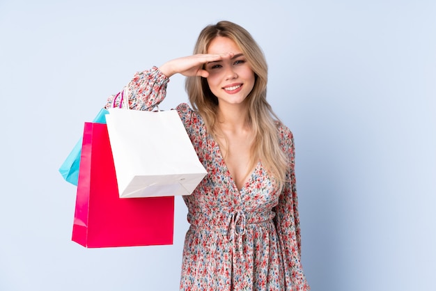 Chica adolescente con bolsa aislado en la pared azul mirando lejos con la mano para mirar algo