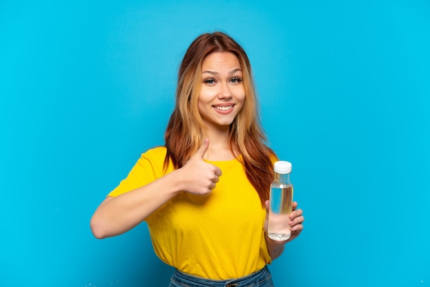 Chica adolescente con una botella de agua sobre fondo azul aislado dando un gesto de pulgar hacia arriba