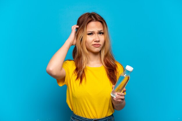 Chica adolescente con una botella de agua sobre fondo azul aislado teniendo dudas